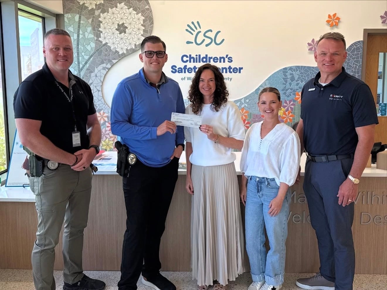 Five people, two women and three men, posing with a large check at the Children's Safety Center.